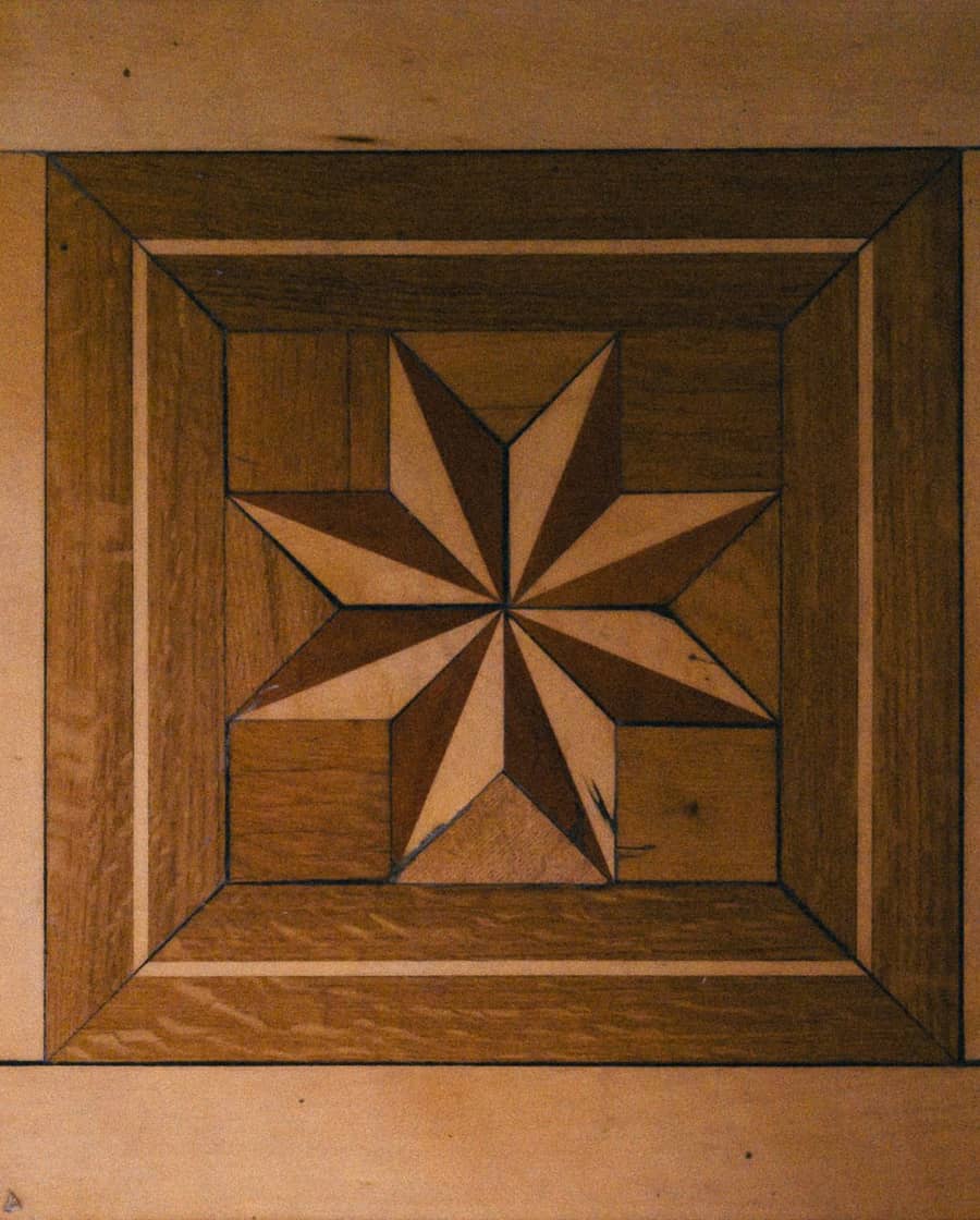 Eingelegter Stern aus hellem und dunklem Holz in einem alten Parkettboden. Beispielfoto.